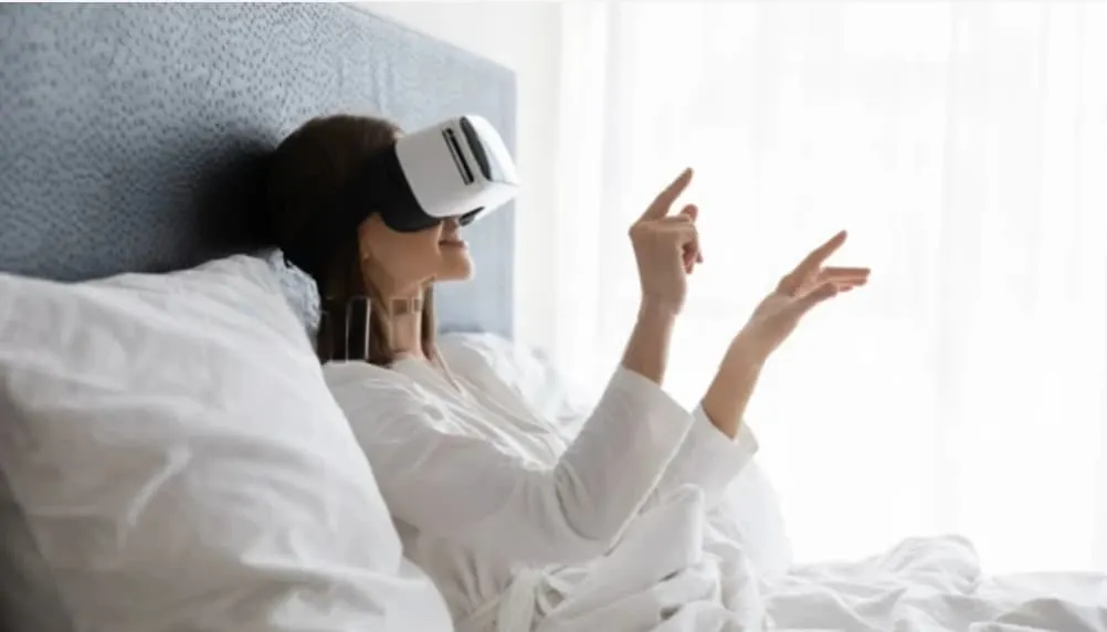 Traveller in bed wearing a virtual reality headset and reaching out to browse in mid-air